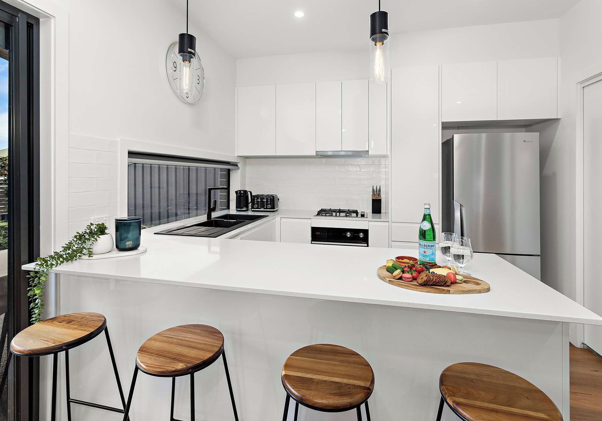 A modern kitchen with a central island, bar stools, a refrigerator, and a coffee machine.