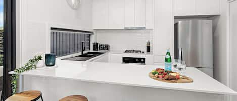 A modern kitchen with a central island, bar stools, a refrigerator, and a coffee machine.