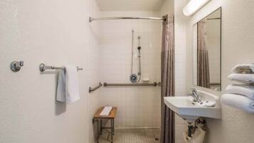 A small, compact bathroom with a shower, a sink, and a mirror.