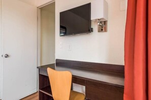 Quarto com escrivaninha, cadeira, televisão fixada na parede e porta.