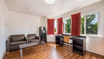 Een moderne woonkamer met een bank, een salontafel, een bureau met een stoel, en een groot raam met gordijnen.