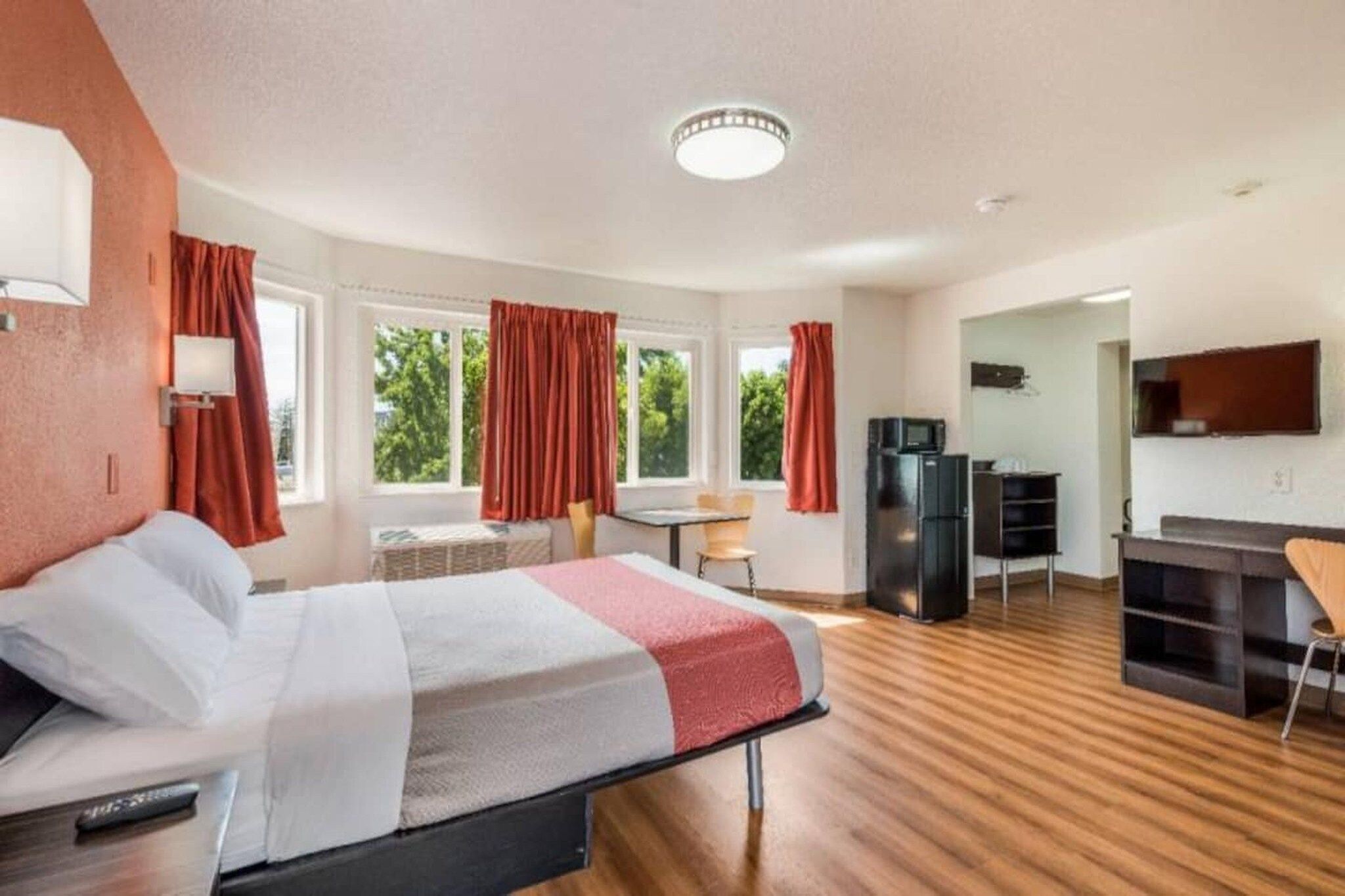 A hotel room with a bed, a desk, a chair, a television, and a refrigerator.