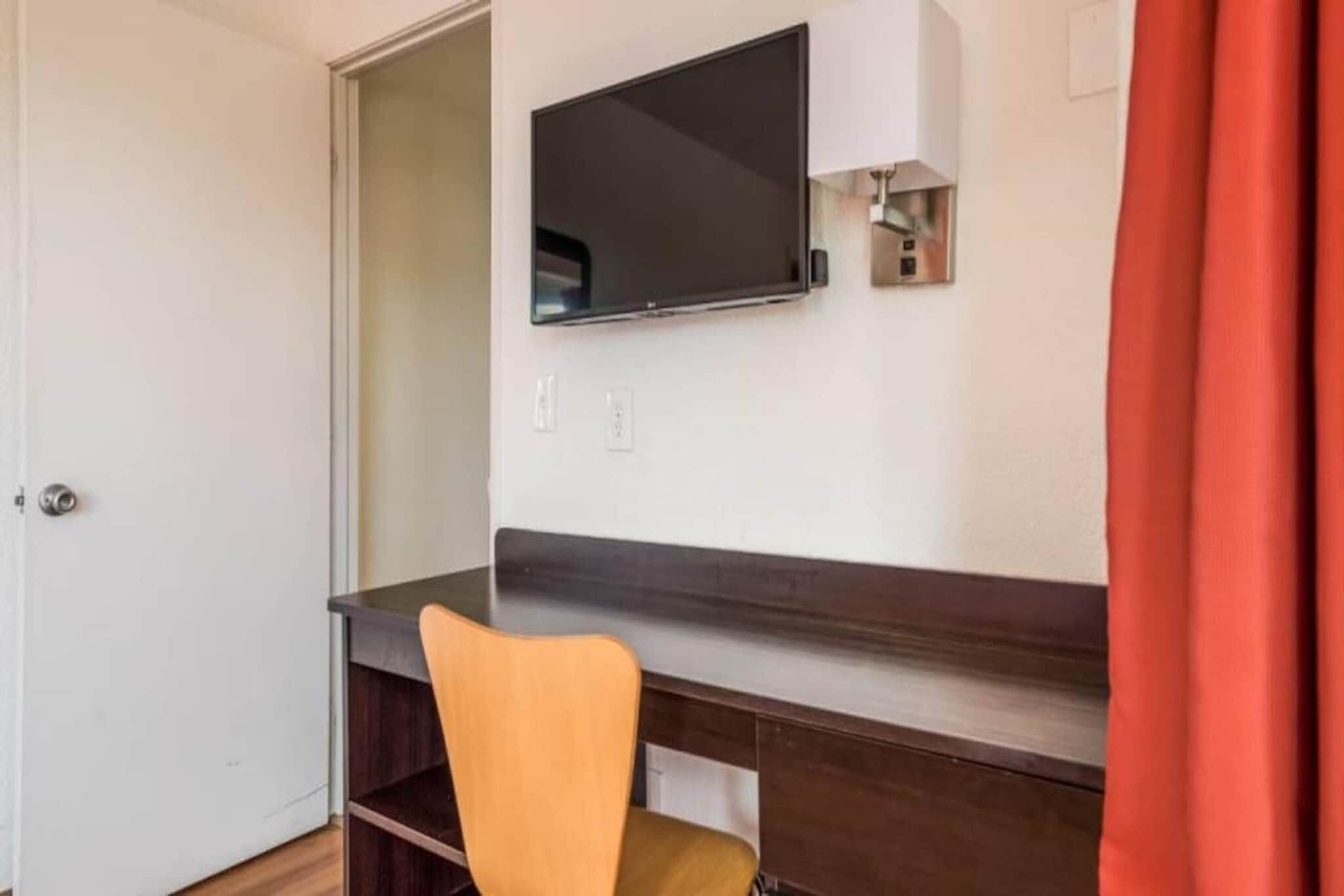 A room with a desk, a chair, a television mounted on the wall, and a door.