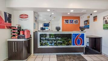 A reception desk with a digital screen displaying a message, a coffee station, and a wall with framed pictures.