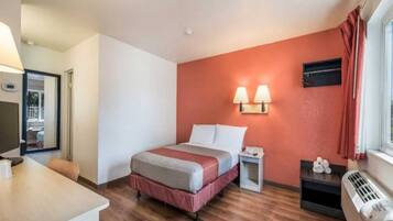 Quarto de hotel com cama, mesa de cabeceira, abajur e janela com cortinas.