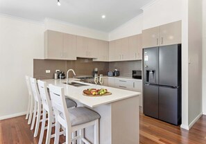 Une cuisine moderne dotée d’un îlot central, de chaises blanches, d’un réfrigérateur noir et de divers appareils électroménagers.