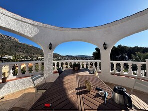 Eine Terrasse im Freien mit Holzboden, weißen Geländern und Blick auf eine gebirgige Landschaft.