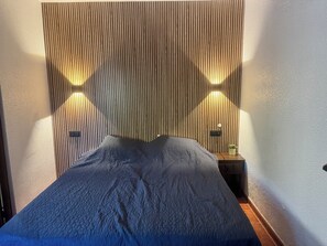 Ein Bett mit blauer Strukturdecke, einem Holz-Schlafkopf und zwei an der Wand befestigten Leuchten auf jeder Seite.