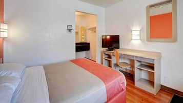 A hotel room with a bed, a desk with a chair, a television, and a mirror.