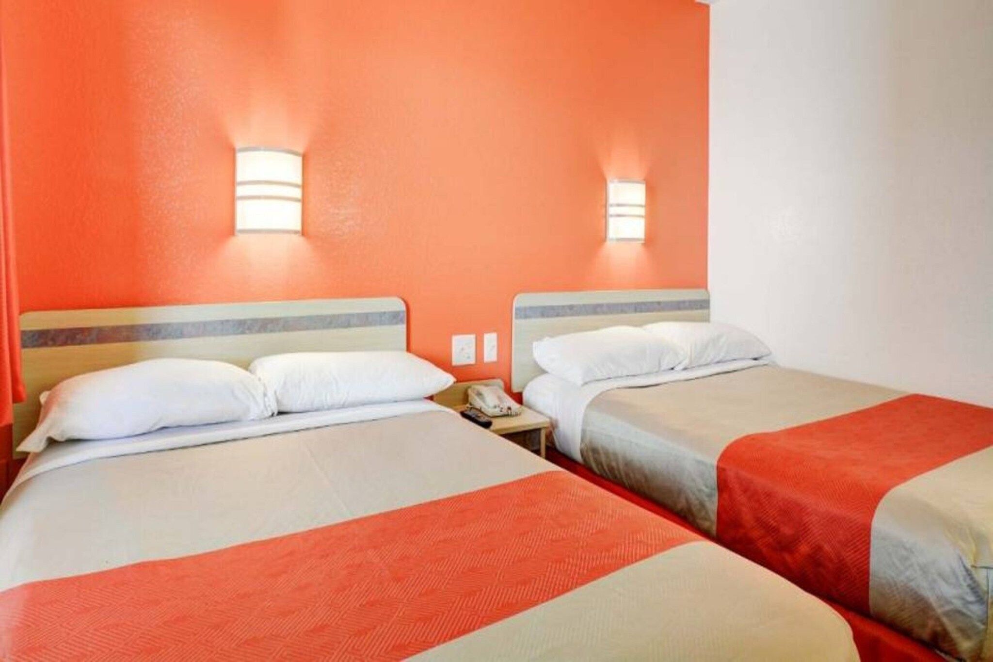 Une chambre d’hôtel avec deux lits, chacun recouvert d’une courtepointe rouge et blanche, et deux appliques murales.