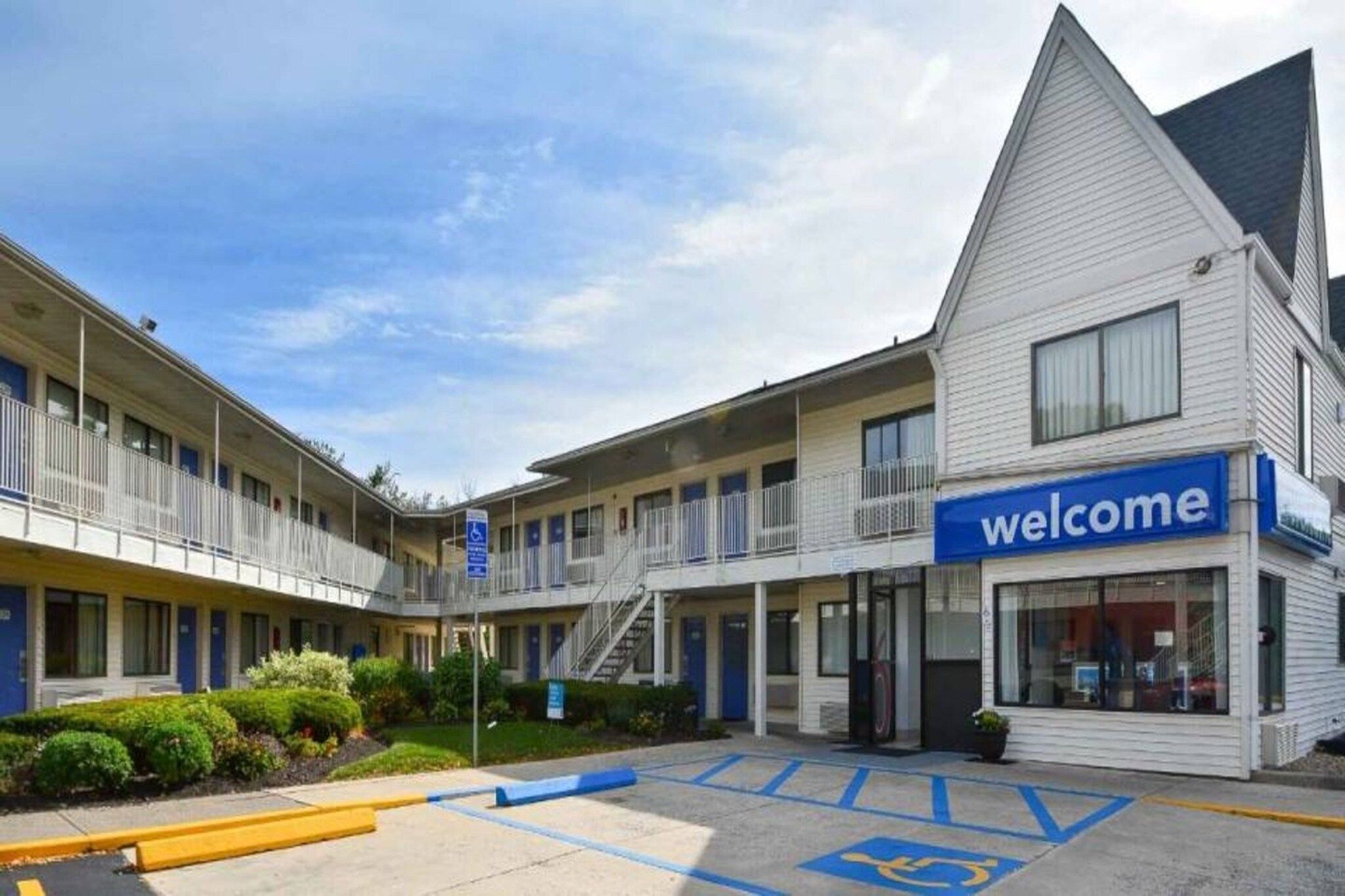 Un motel con un cartel de 'welcome', varias habitaciones, un estacionamiento y una plaza de aparcamiento adaptada para personas con discapacidad.