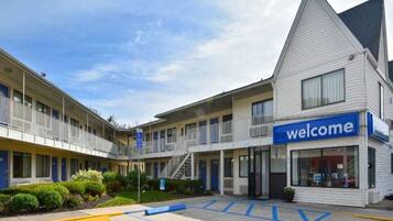 Un motel con un cartel de 'welcome', varias habitaciones, un estacionamiento y una plaza de aparcamiento adaptada para personas con discapacidad.