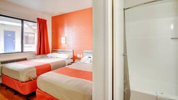 Ein Hotelzimmer mit zwei Betten, einer Dusche und einem Fenster mit Vorhängen.