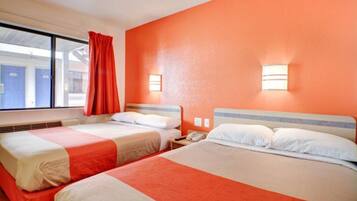 Una camera d'albergo con due letti, una finestra con tende rosse e un punto luce fissato al muro.