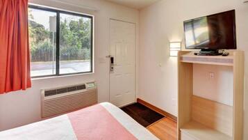 A hotel room with a bed, a television on a stand, a door, and a window with curtains.