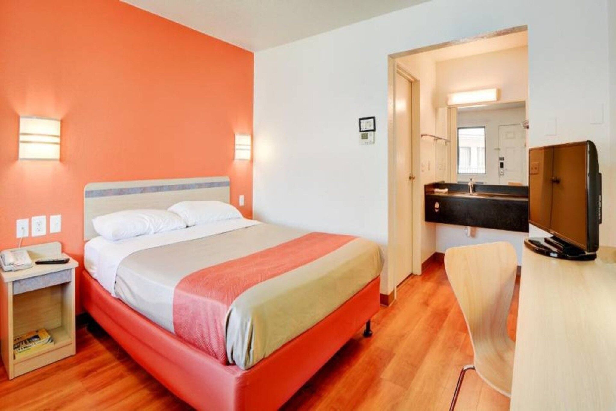A hotel room with a bed, bedside table, and a desk with a chair.