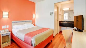 A hotel room with a bed, bedside table, and a desk with a chair.