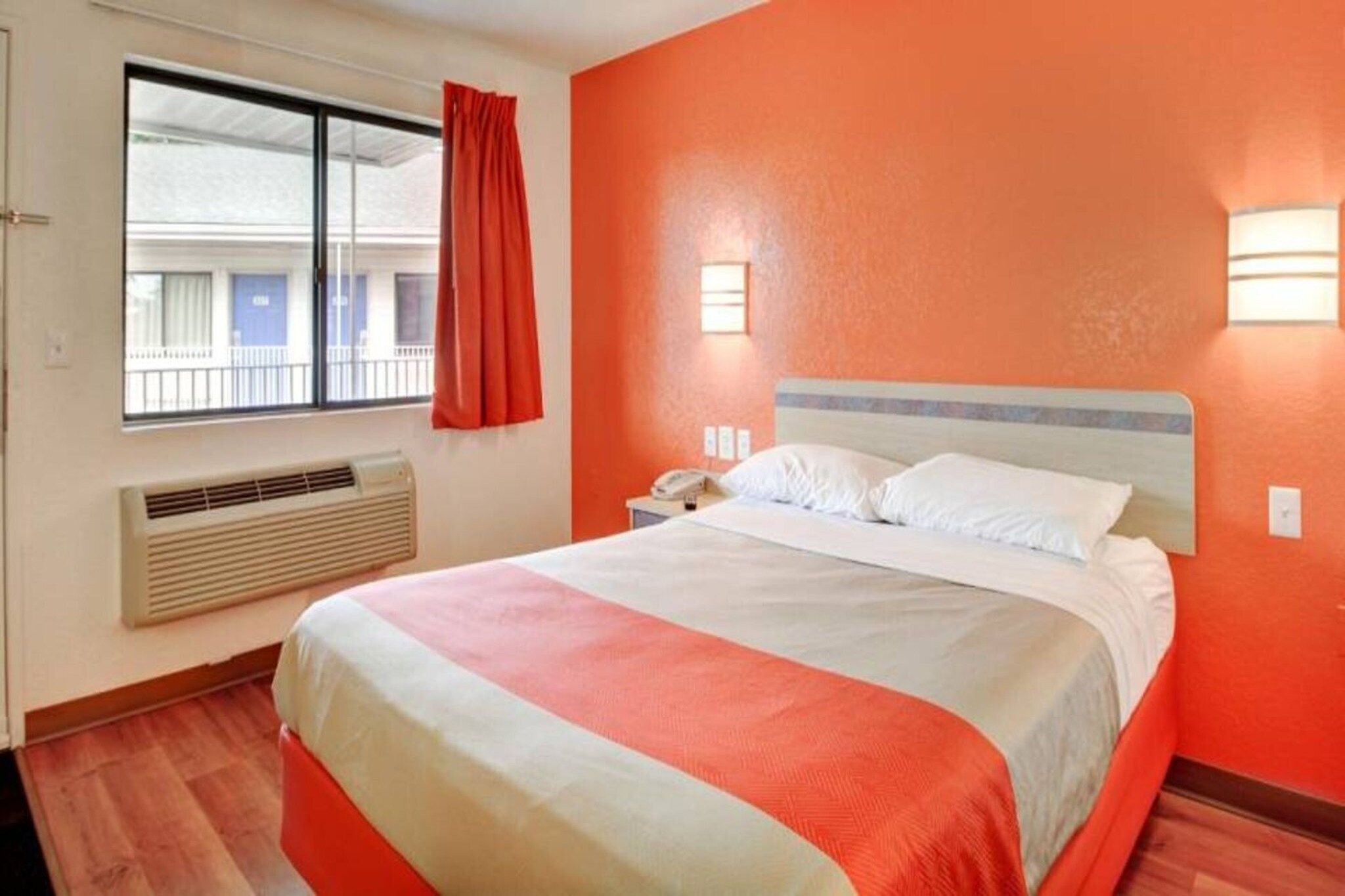 Une chambre d’hôtel avec un lit, une fenêtre avec des rideaux, un radiateur et une table de chevet avec un téléphone.