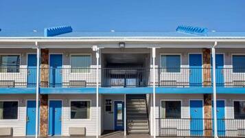 Ein mehrstöckiges Motel mit einem zentralen Eingang, Balkonen und einem Parkplatz.