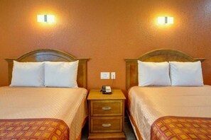 A hotel room with two beds, each with a headboard, a bedside table with a phone, and a wall socket.