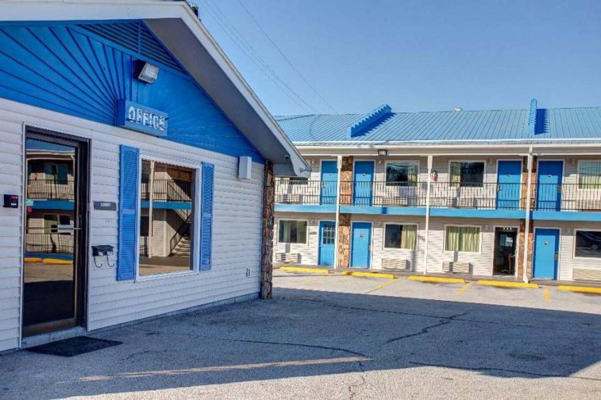 A motel with a blue and white exterior, a covered parking area, and a two-story building with multiple rooms.