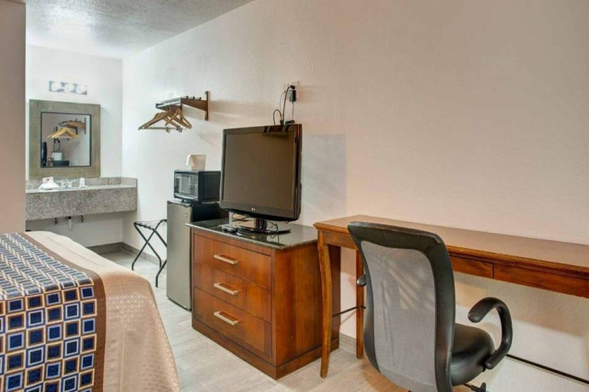 Hotellihuone, jossa on sänky, työpöytä tietokoneella, tuoli, televisio ja pieni keittokomero.