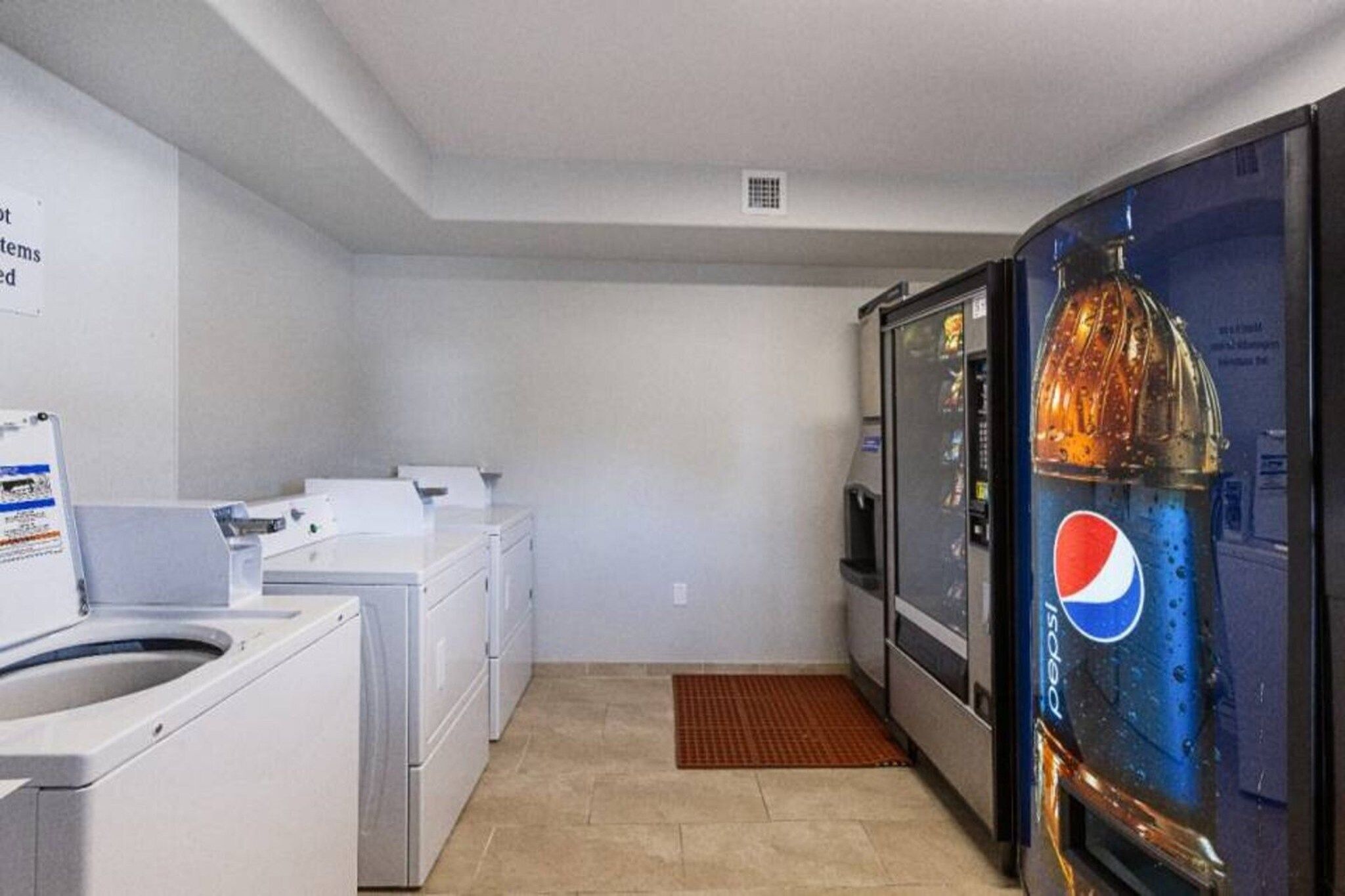 A laundry room with a washing machine, dryer, and a refrigerator with a Pepsi logo.