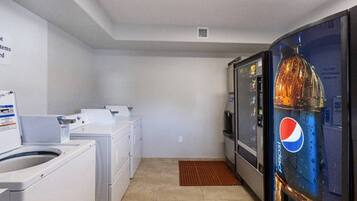 A laundry room with a washing machine, dryer, and a refrigerator with a Pepsi logo.
