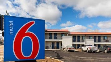 A motel sign with the number 6, a parking lot, and a building with multiple windows and a red roof.
