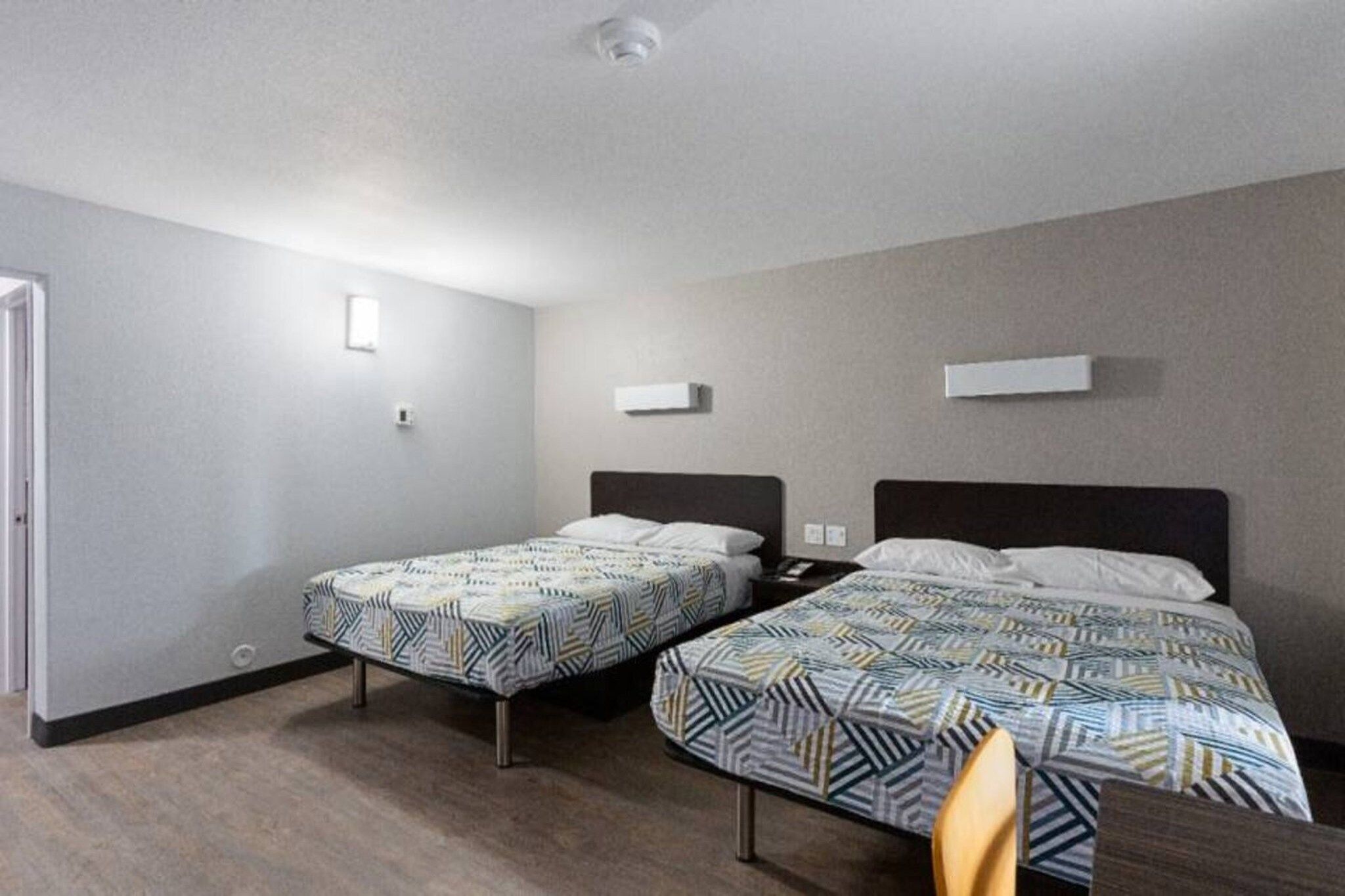 A hotel room with two beds, a nightstand, a chair, and a door.