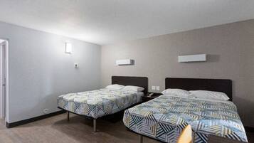 A hotel room with two beds, a nightstand, a chair, and a door.