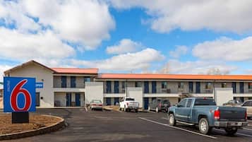 Ein Motel mit rotem Dach, mehreren Zimmern und einem Parkplatz mit einigen Fahrzeugen.