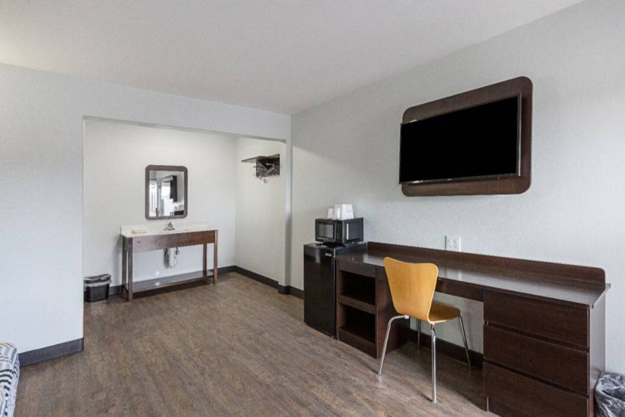 Ein Hotelzimmer mit Holzboden, einem Schreibtisch mit Stuhl, einem an der Wand befestigten Flachbildfernseher und einem kleinen Tisch mit Spiegel.