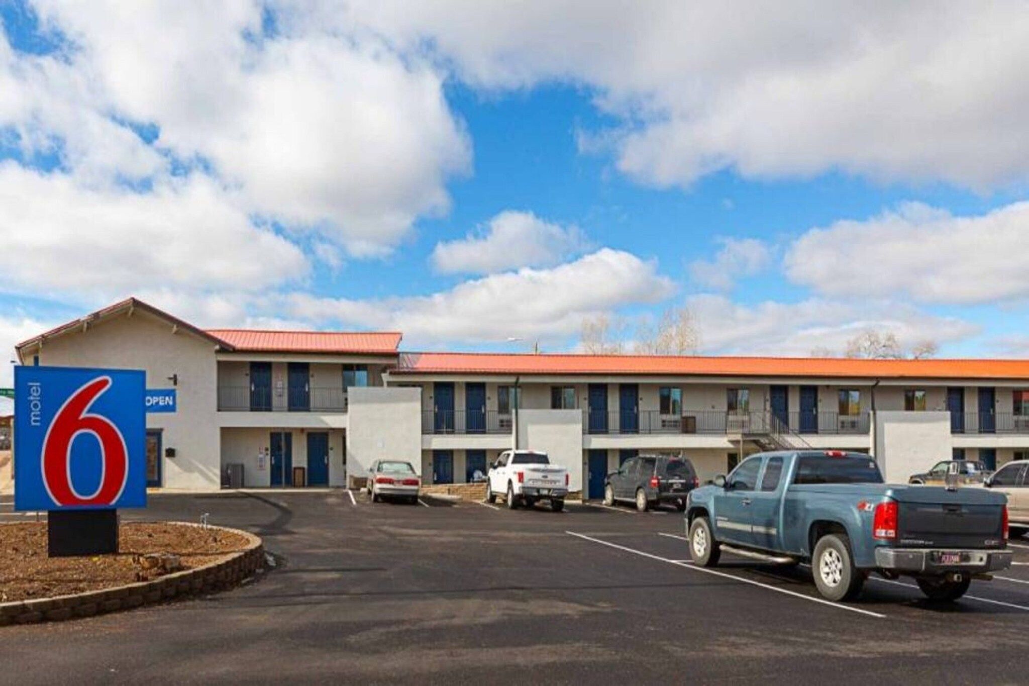 A motel with a red roof, multiple rooms, and a parking lot with several vehicles.