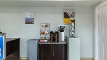 A reception area with a coffee machine, trash bin, and a bulletin board on the wall.