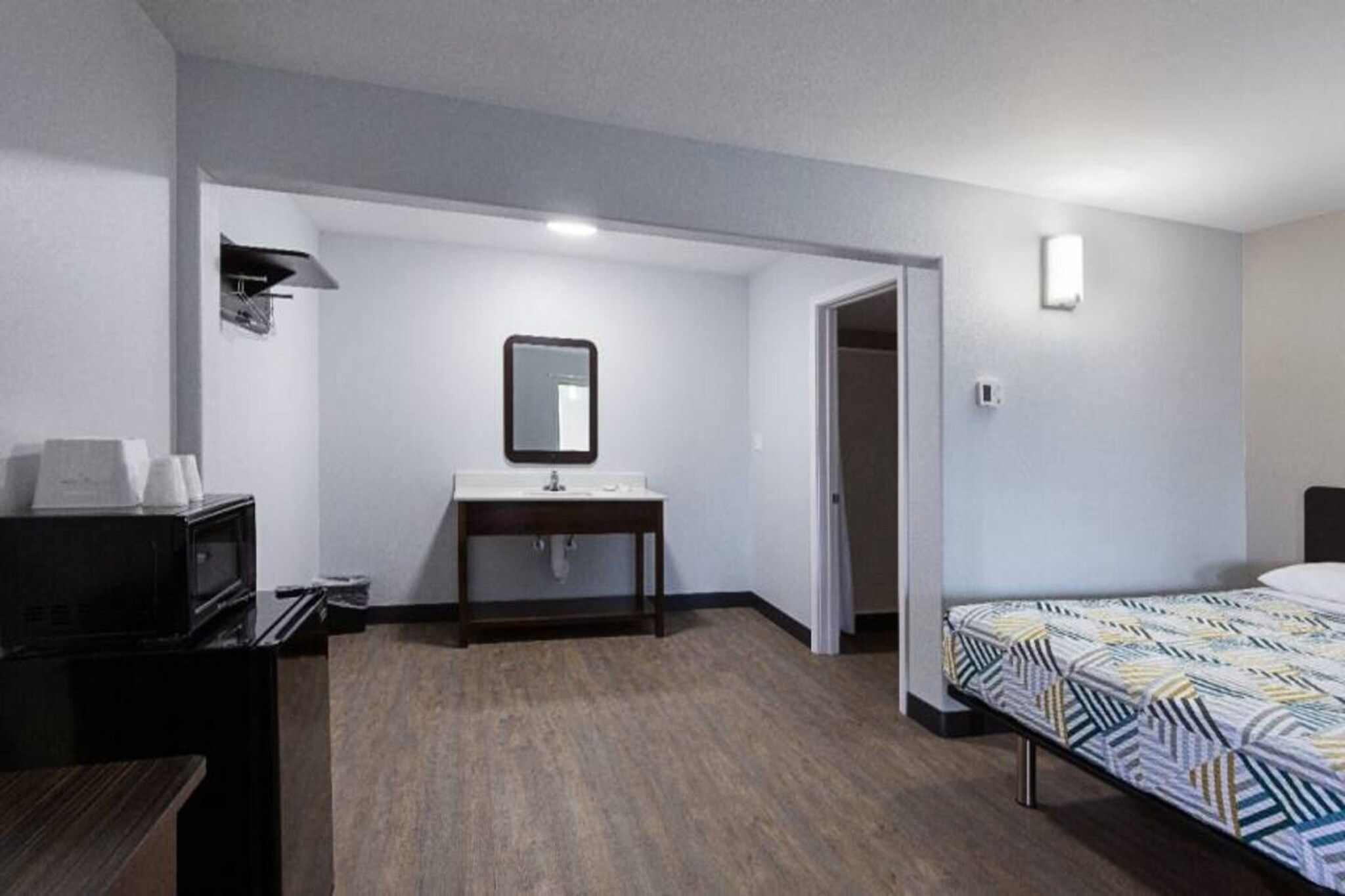 A hotel room with a bed, a desk, a mirror, a television, and a door leading to another room.