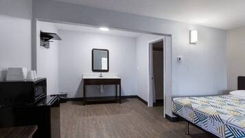 A hotel room with a bed, a desk, a mirror, a television, and a door leading to another room.