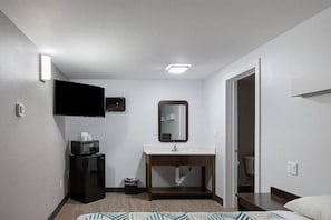 A hotel room with a bed, a bedside table, a mirror, a sink, and a refrigerator. - 1 King Bed | Non-Smoking, Micfridge (Show Low)