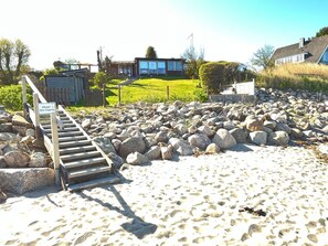 A beach with a wooden staircase leading to a private area, surrounded by large rocks and a grassy field. - fewo1846 - Utkiek / Three-bedroom vacation home with private beach access (Glücksburg (Ostsee))