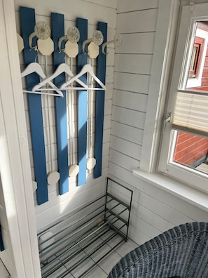 Ein Zimmer mit weißer Wand, einem Fenster mit Jalousien, einem Metallgestell und einem Kleiderhaken mit weißen Kleiderbügeln und Dekorationen.