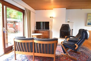Ein Wohnzimmer mit einer Couch, einem Schaukelstuhl, einem Fernseher, einem Kamin und einem großen Fenster.