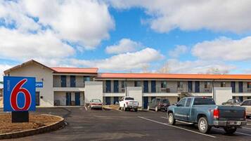Un motel con techo rojo, varias habitaciones y un estacionamiento con varios vehículos.