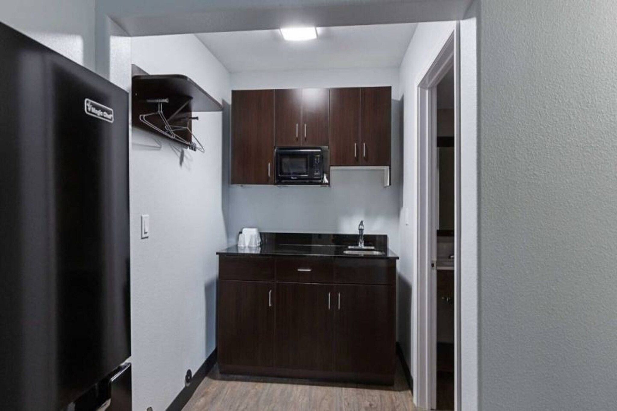A compact kitchen with dark cabinets, a microwave, and a refrigerator.