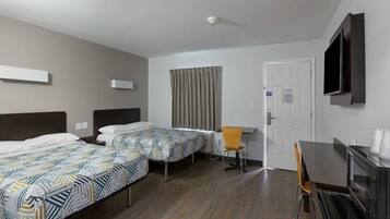 A hotel room with two single beds, a desk, a chair, a TV mounted on the wall, and a door.