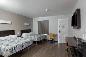 Une chambre d’hôtel avec deux lits simples, un bureau, une chaise, un téléviseur fixé au mur et une porte.