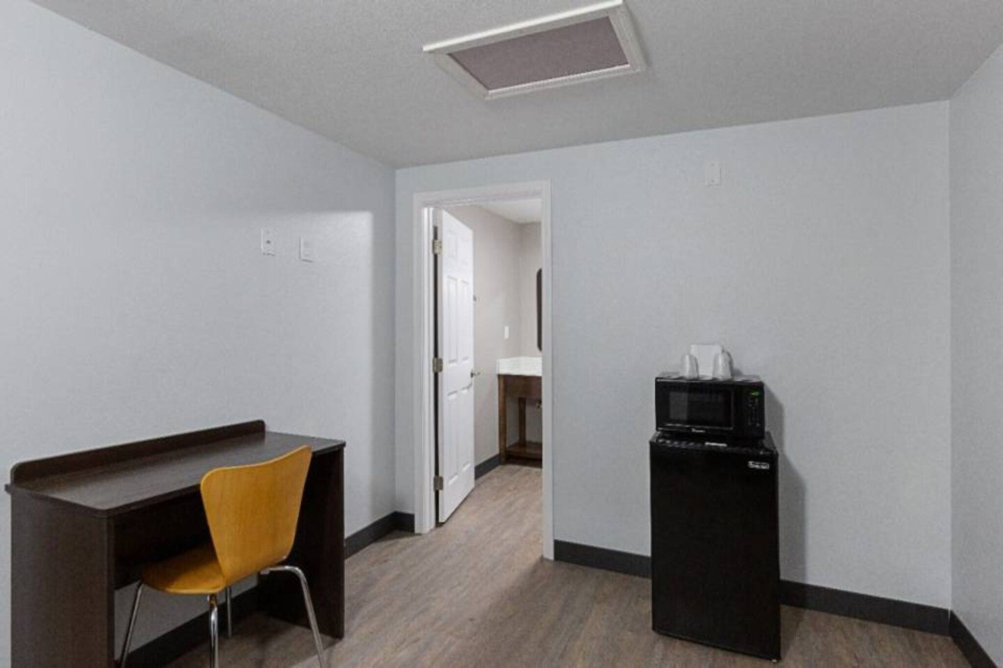 Ein Hotelzimmer mit Schreibtisch, einem Sessel, einer Mikrowelle und einer Tür zu einem anderen Raum.