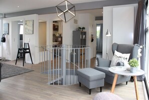A modern living room with a grey sofa, a small round table, and a staircase with a glass railing. - fewo1846 - StrandNest - House with a view of the fjord, a fireplace, a sauna, and 3 bedrooms - (Glücksburg (Ostsee))
