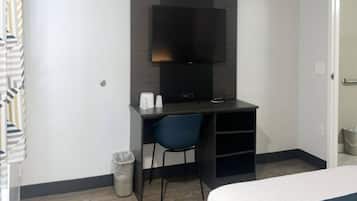 A hotel room with a bed, a desk with a chair, a television, and a trash bin.