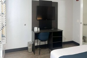 Ein Hotelzimmer mit einem Bett, einem Schreibtisch mit Stuhl, einem Fernseher und einem Mülleimer.