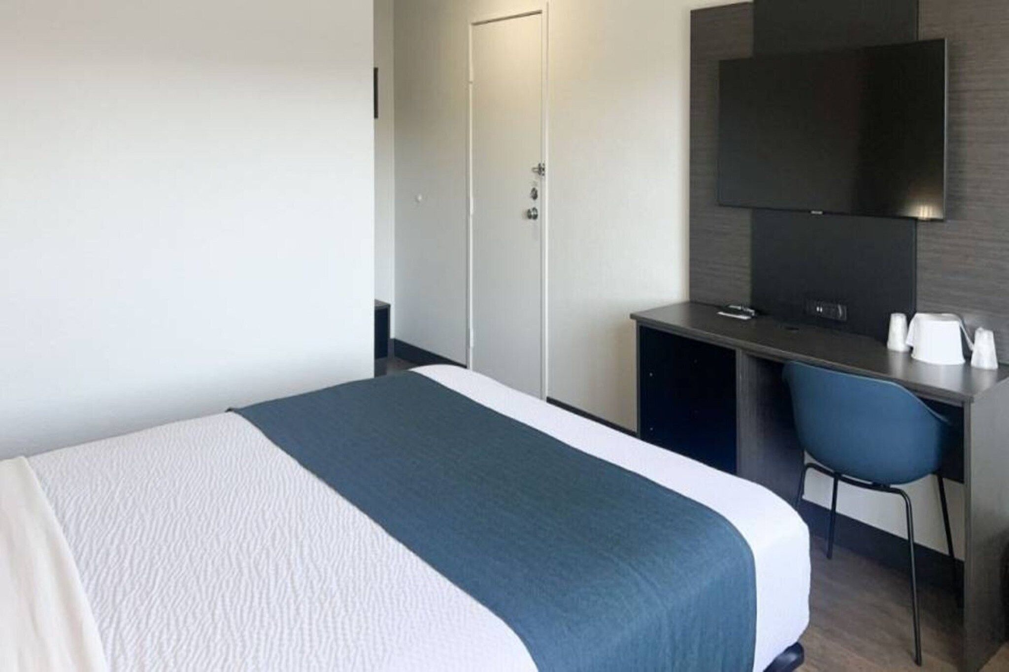 Une chambre d’hôtel comprenant un lit, un bureau, une chaise, une télévision et une armoire.